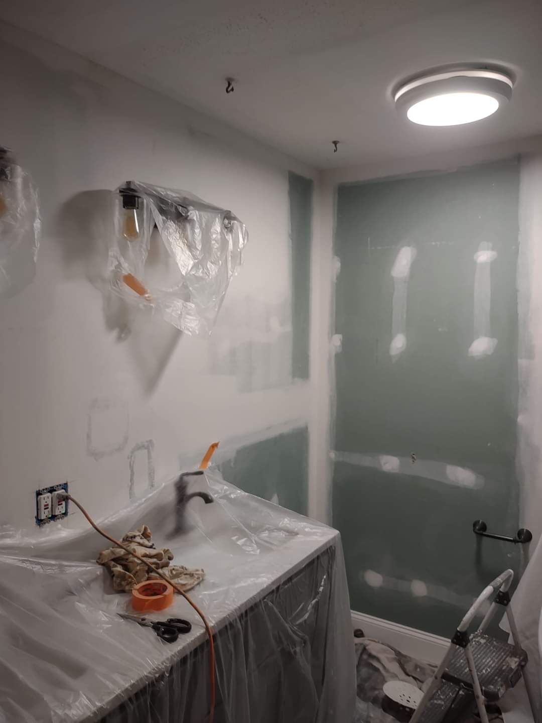 Partially renovated bathroom with sink, covered vanity, and green shower wall being painted.