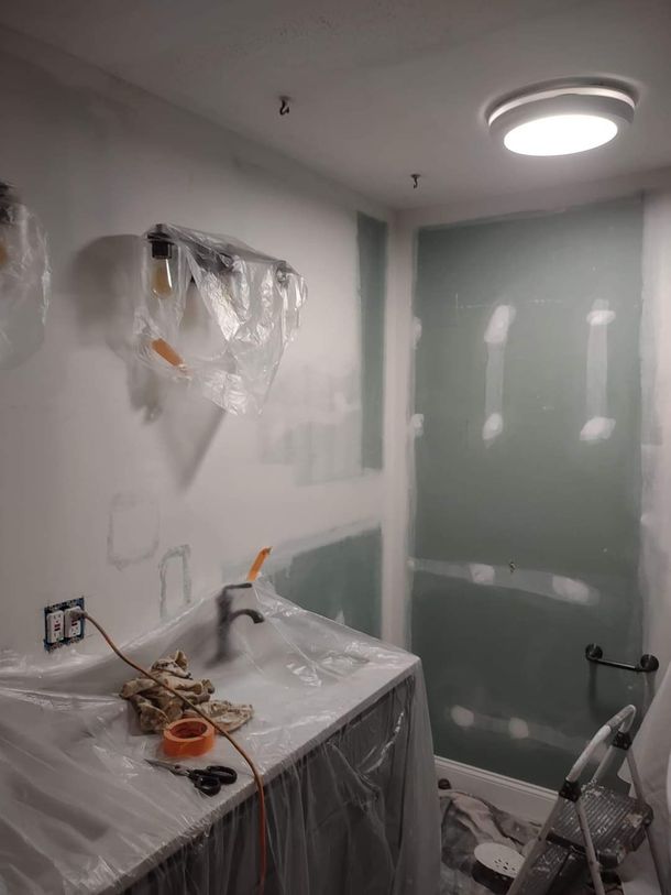 Person sanding a ceiling with a vacuum-equipped pole in a room under renovation