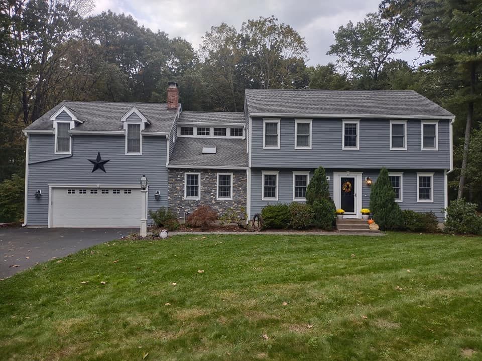 Gray two-story suburban house with white trim, front lawn, and attached garage under overcast sky