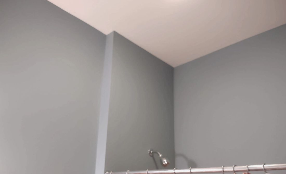 Gray bathroom corner with white trim and a shower curtain rod visible near the ceiling