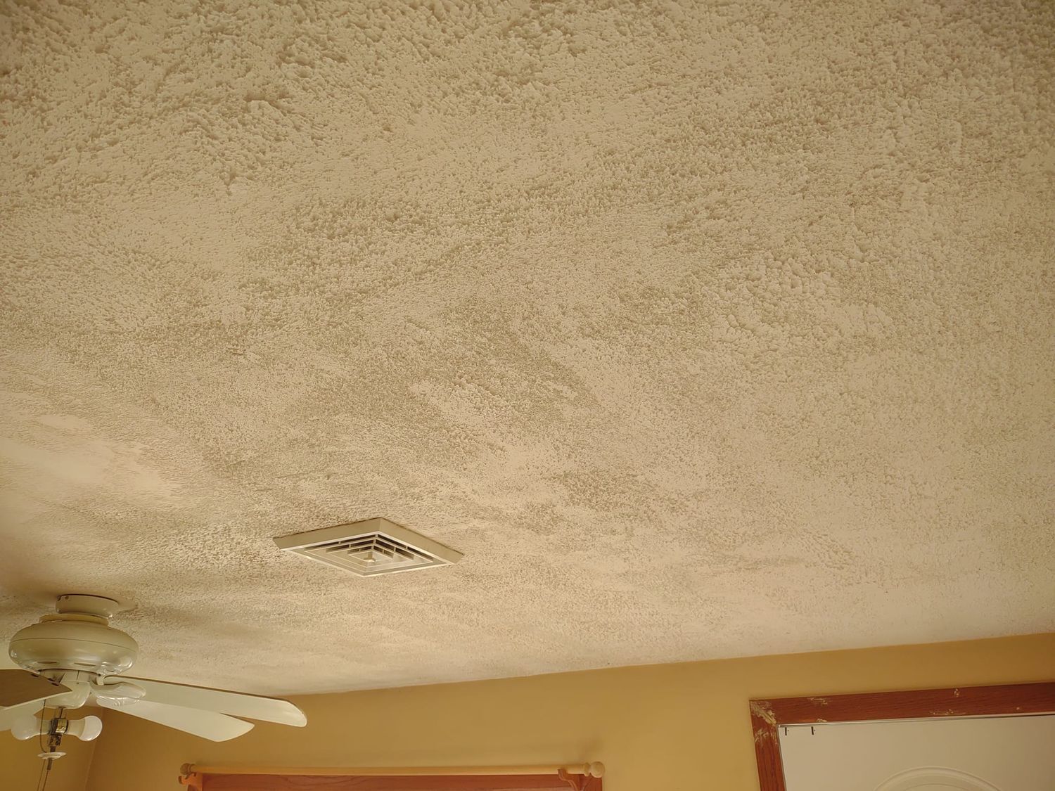 Stained popcorn ceiling with a hole and water damage above a ceiling fan and wall corner