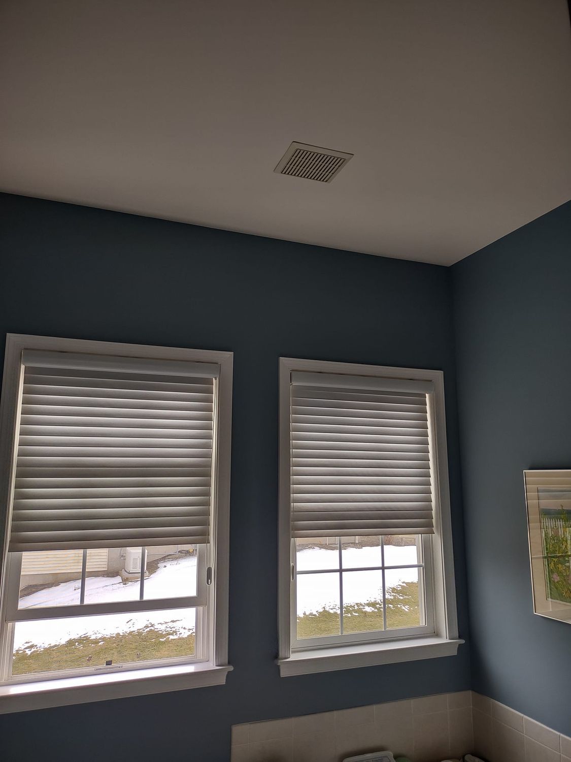 Blue room corner with two windows, gray blinds, and snowy view outside