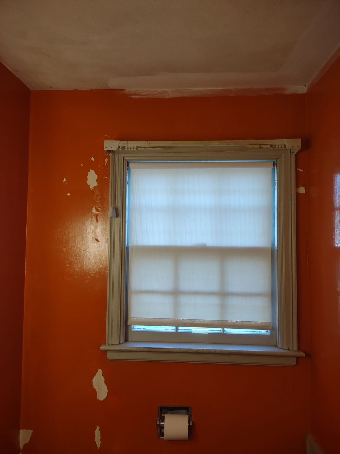 Orange room wall with a small window and white blinds, plus a wall outlet below.