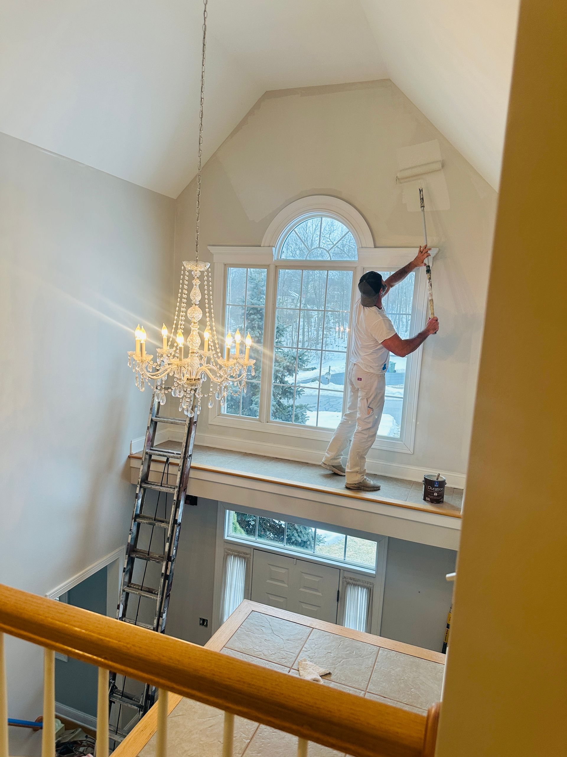 Painter on a ladder painting a vaulted room above a large arched window