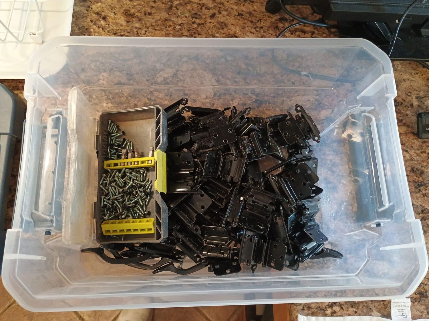 Plastic bin filled with assorted black screws and a small box on a carpeted floor
