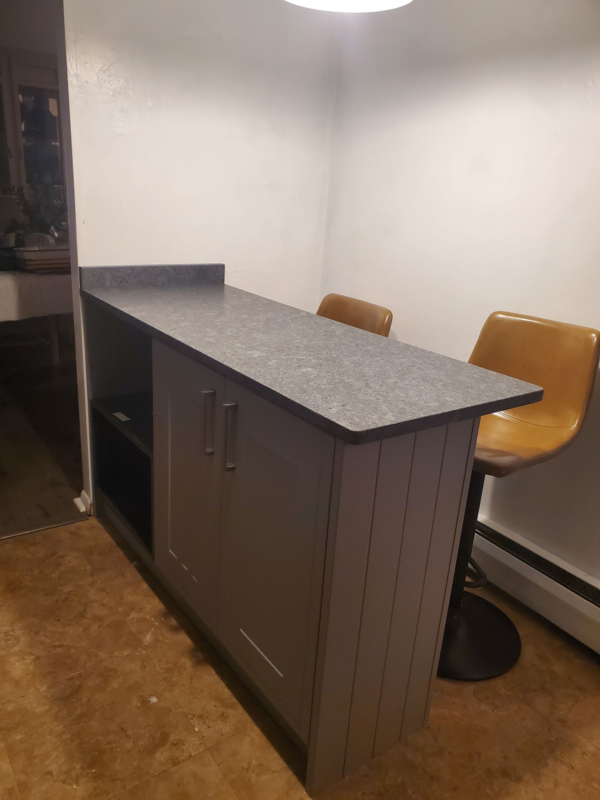 Gray kitchen island with speckled countertop in a small room, with two tan stools beside it.