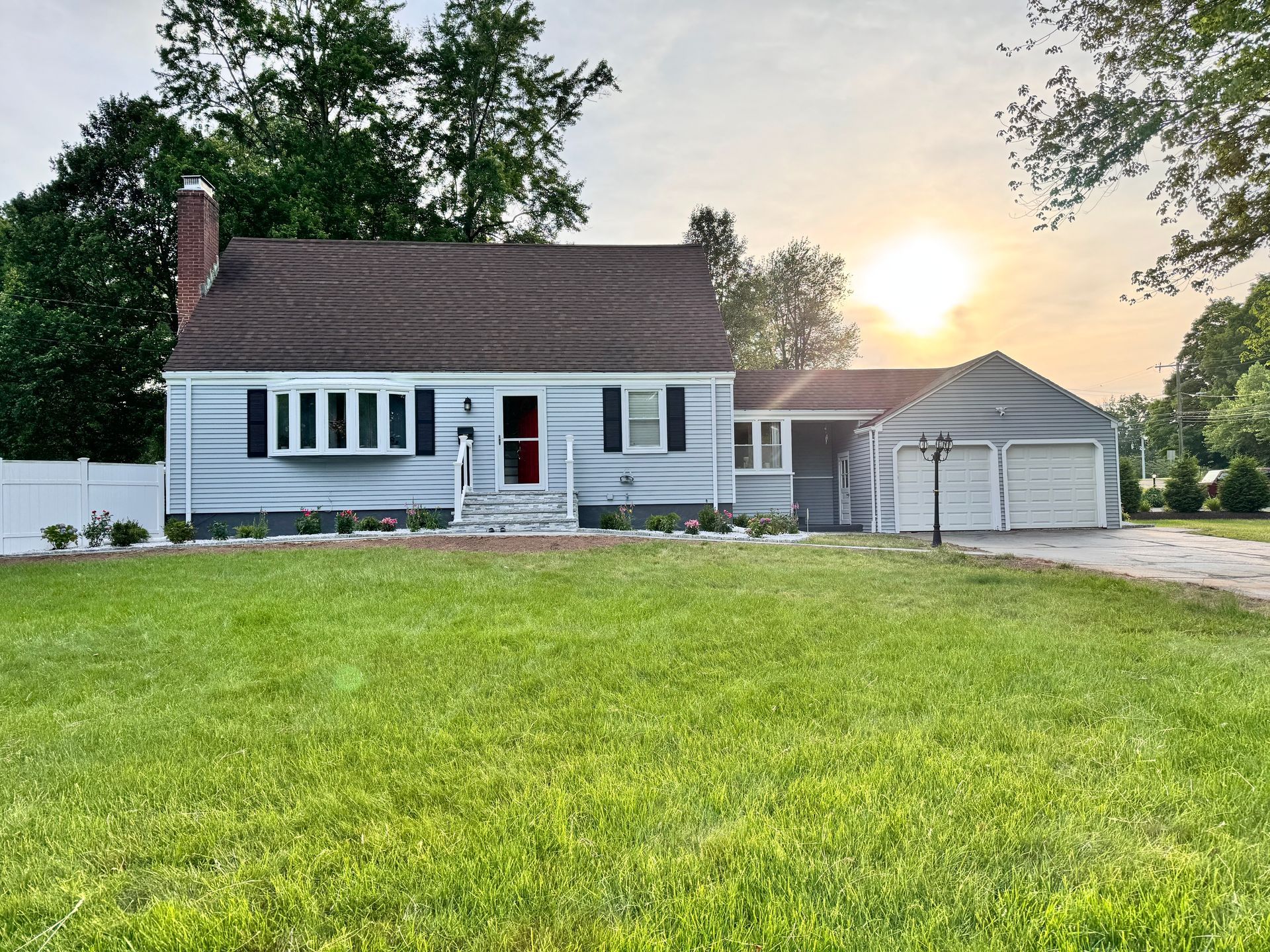 Suburban white house with attached garage at sunset, fronted by a large green lawn.