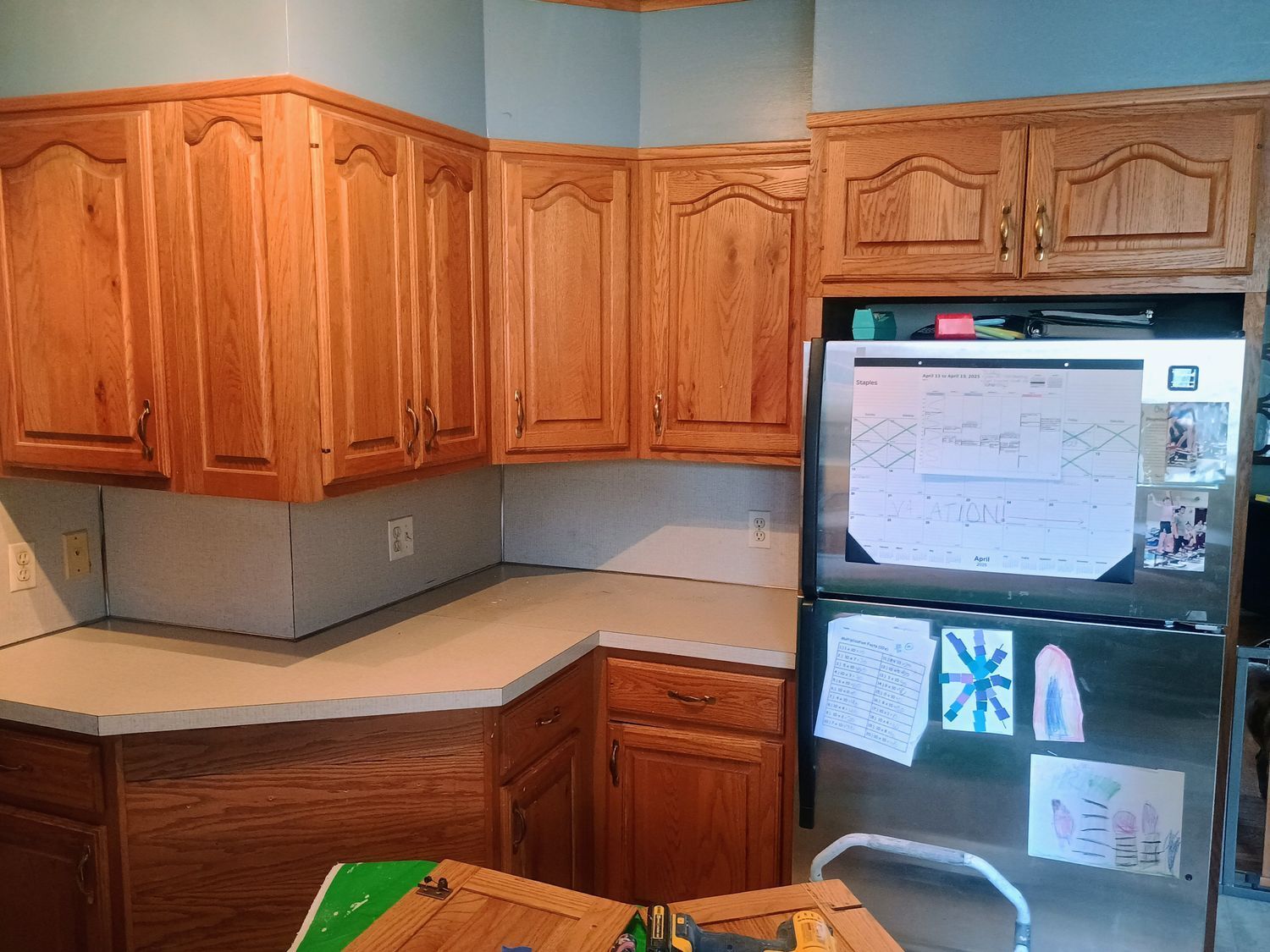 Kitchen with wooden cabinets, light countertops, and a black refrigerator covered in notes and magnets.