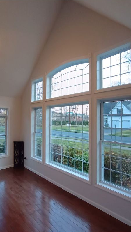 Bright empty room with tall windows, white trim, and polished hardwood floor overlooking a suburban street