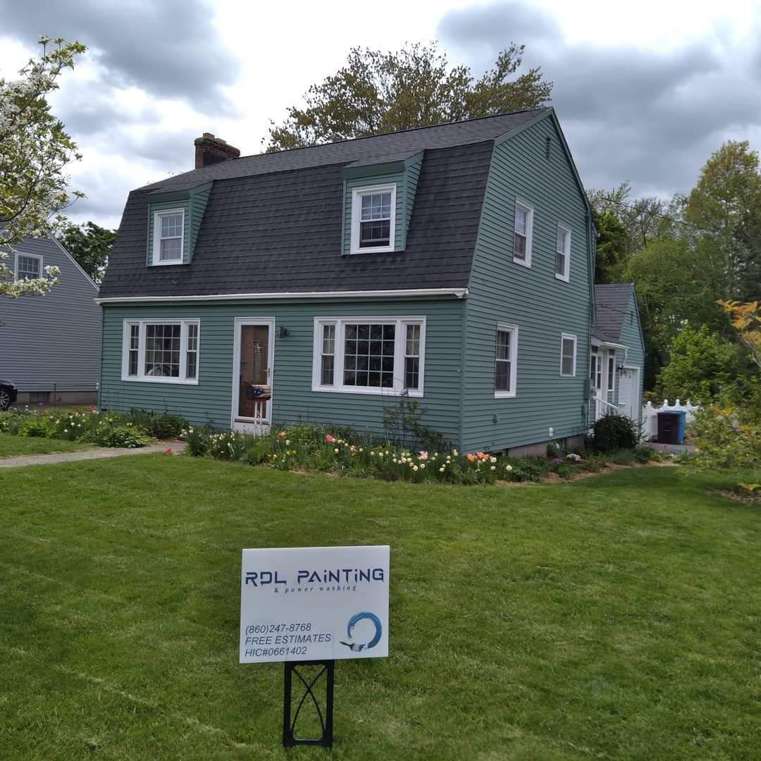 Green two-story house with a lawn and a small sign for a painting service in front