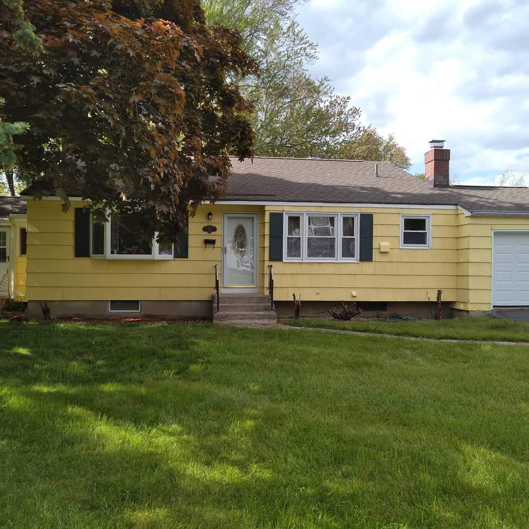 Yellow single-story house with white trim, front porch, and green lawn under a partly cloudy sky