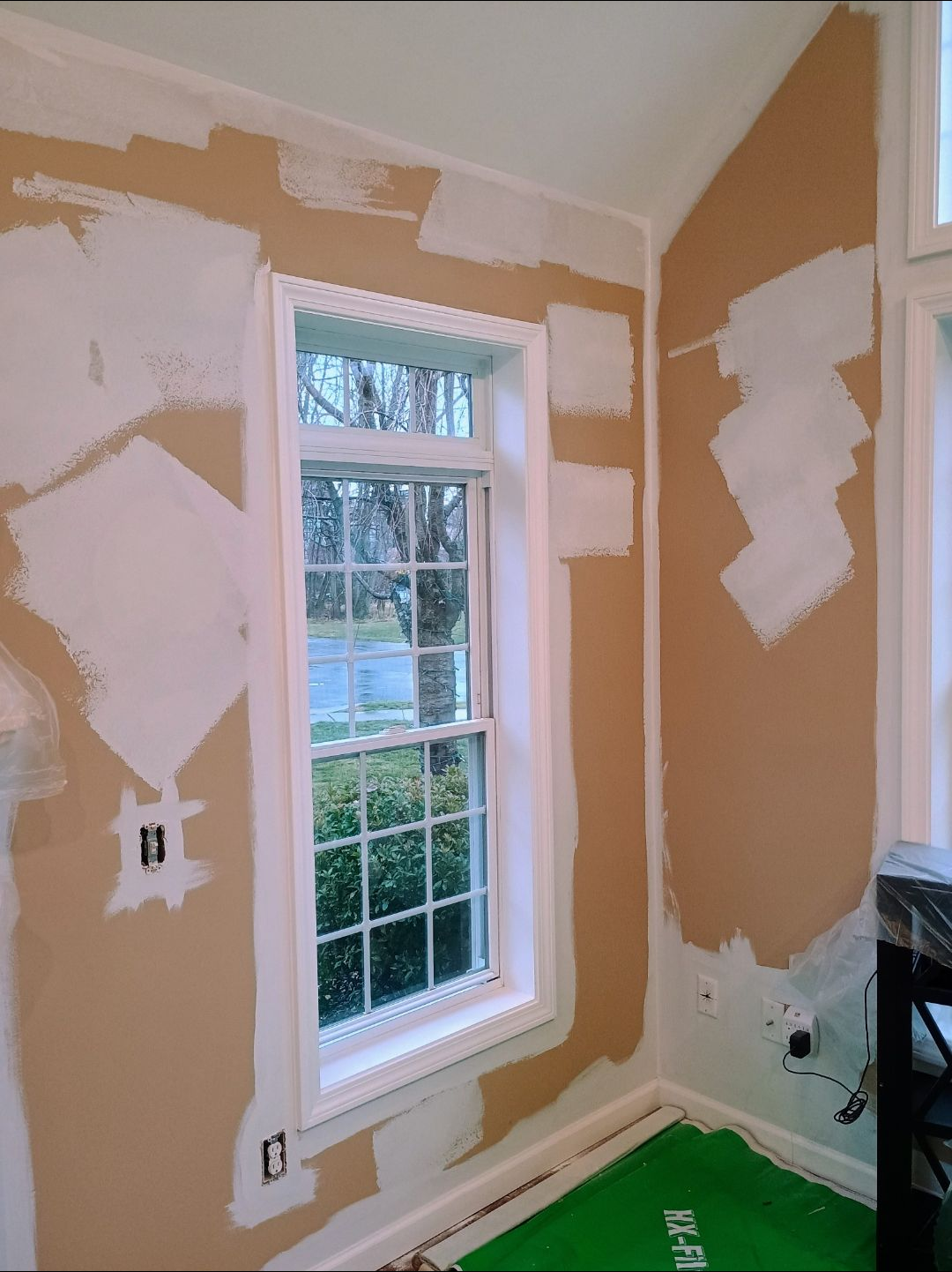 Partially renovated room with tan drywall, white patches, and a window with white trim