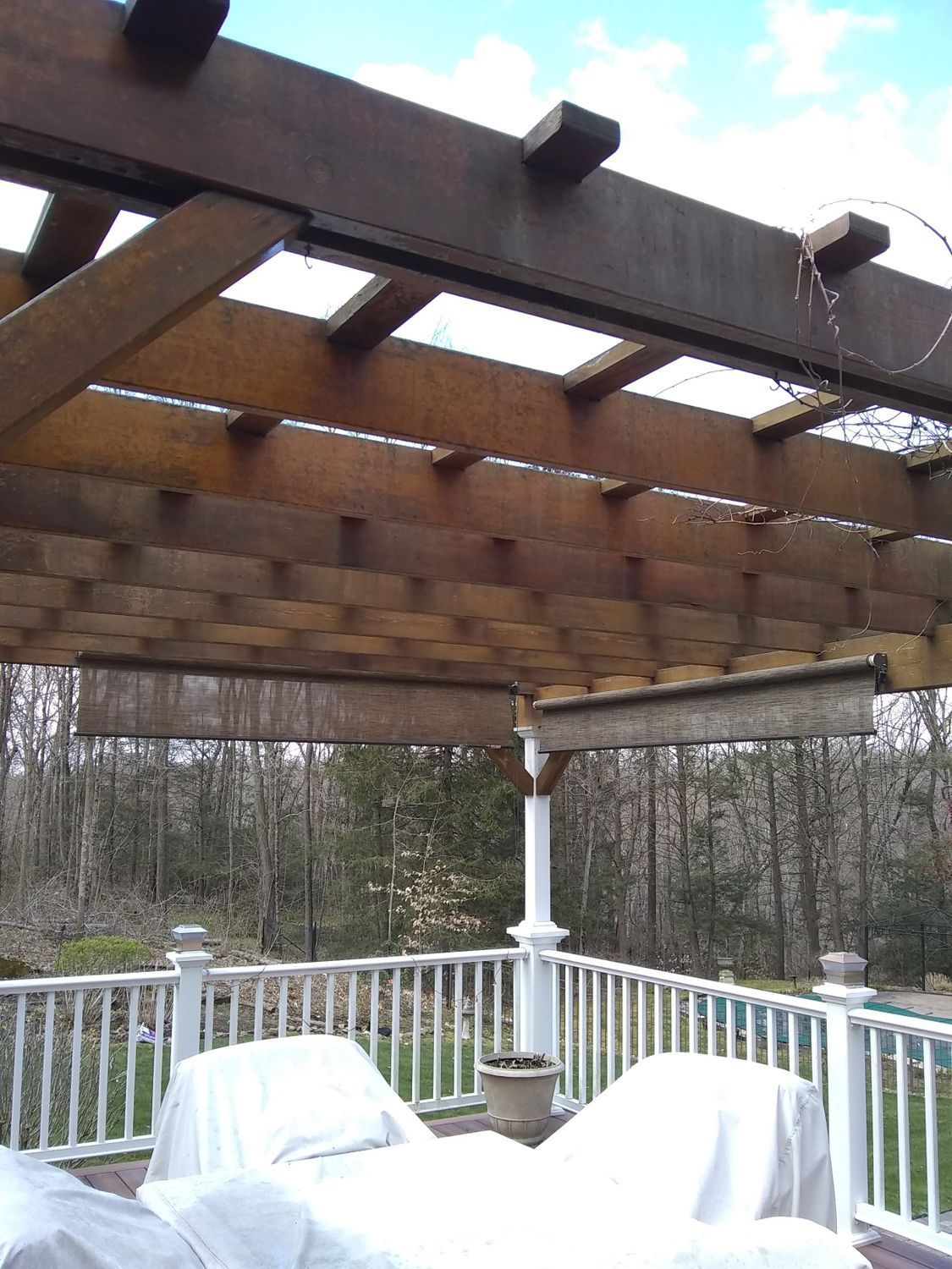 Wooden pergola over a deck with white railing and covered patio furniture overlooking winter trees
