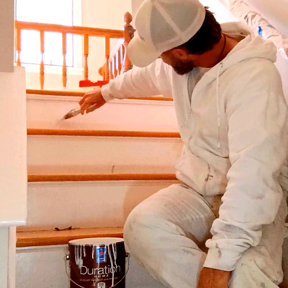 Worker in white coveralls painting a stair railing orange inside a house