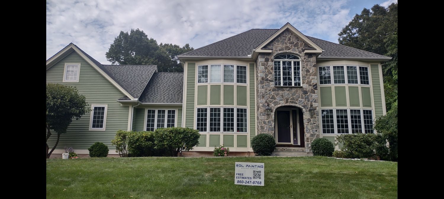 Large two-story house with stone entry, tall windows, and a manicured lawn under cloudy skies