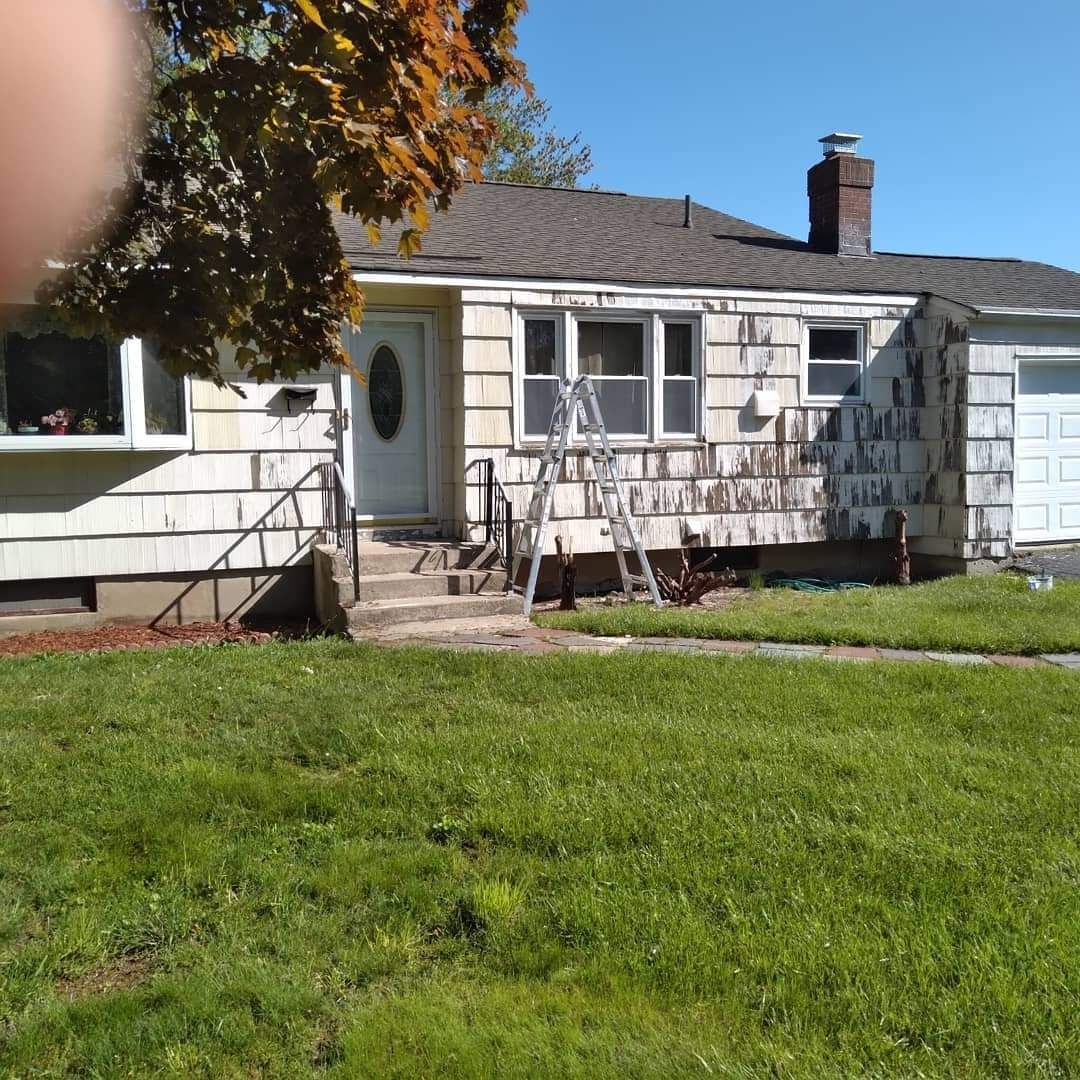 Single-story white house with steps, front lawn, and blue sky, with a finger partly covering the top left corner