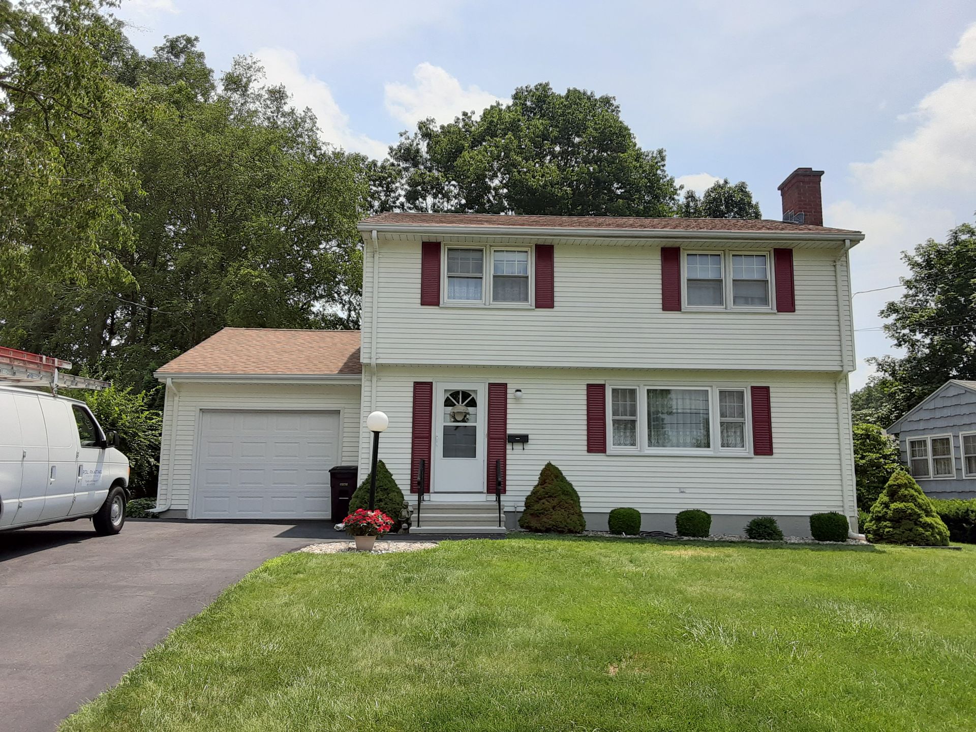 Two-story white house with red shutters, attached garage, and green lawn on a suburban street