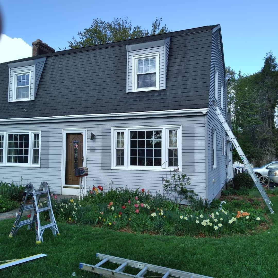 Gray two-story house with white trim, front garden flowers, and a ladder in the lawn.