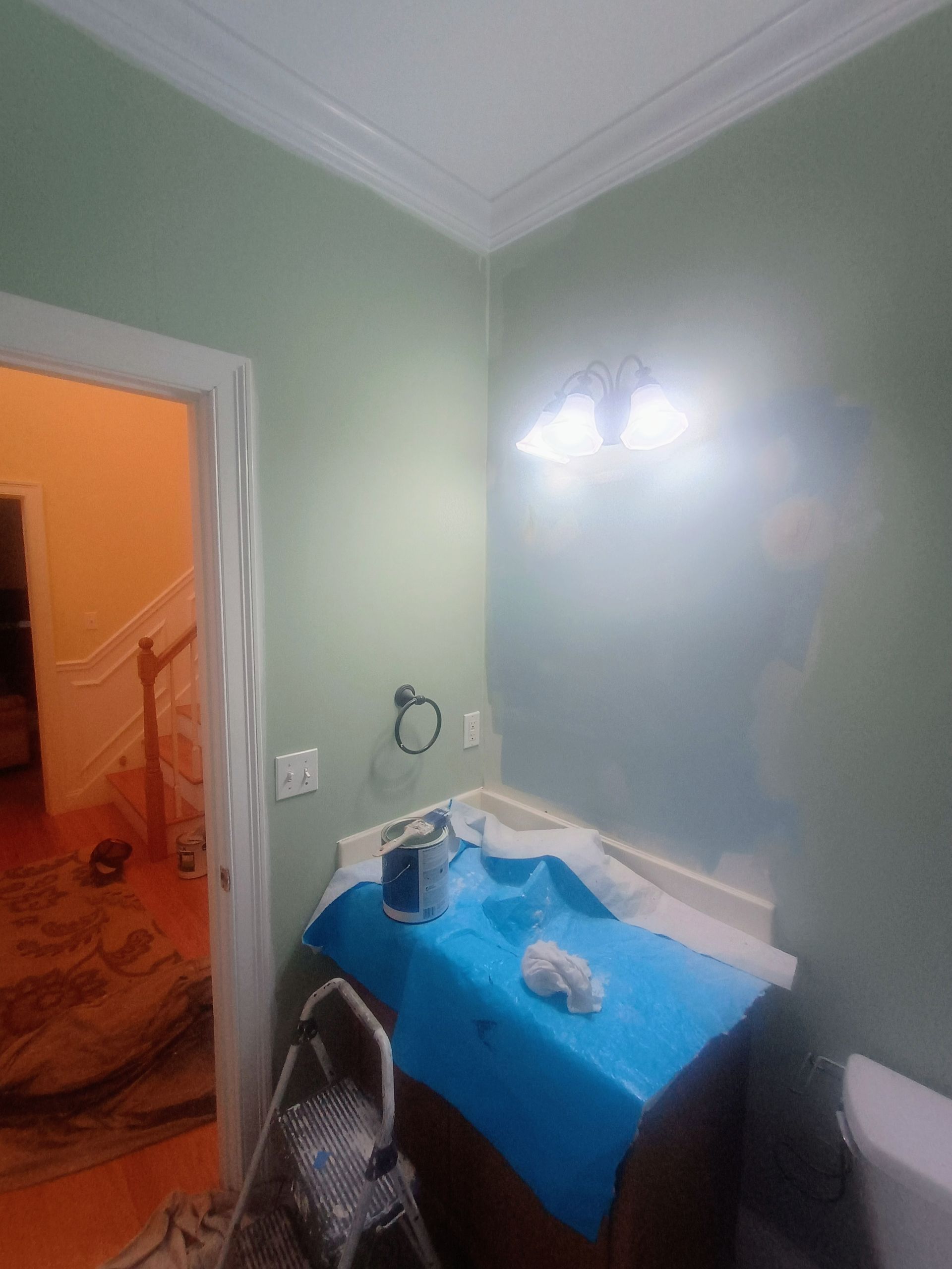 Small bathroom with pale green walls, blue sink cover, mirror, and open doorway to a lit hallway.