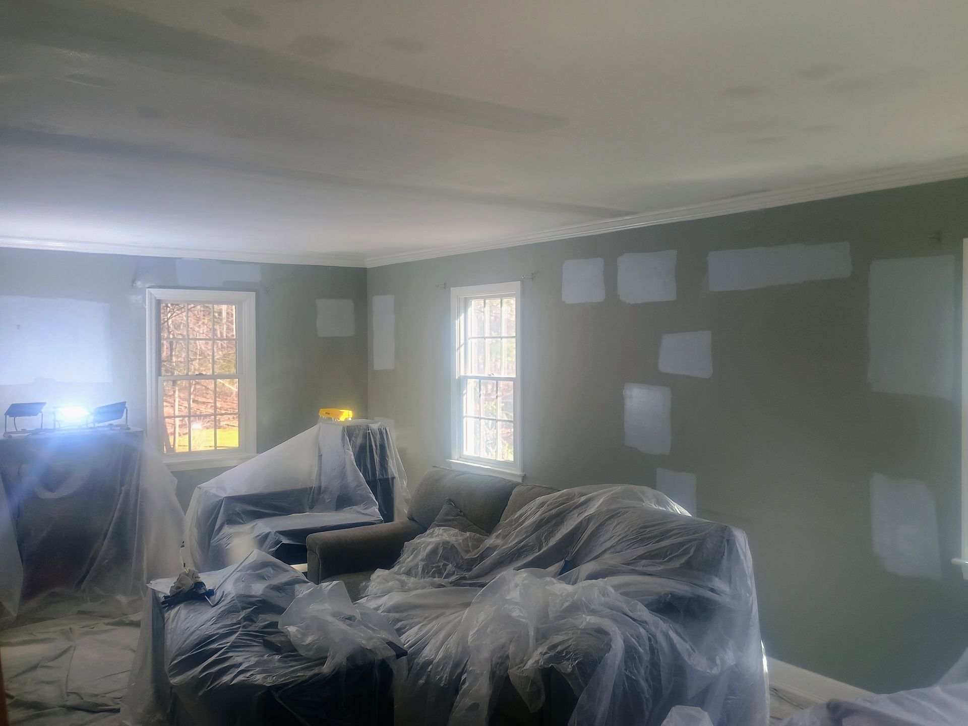 Living room with green walls, windows, and furniture wrapped in plastic during renovation