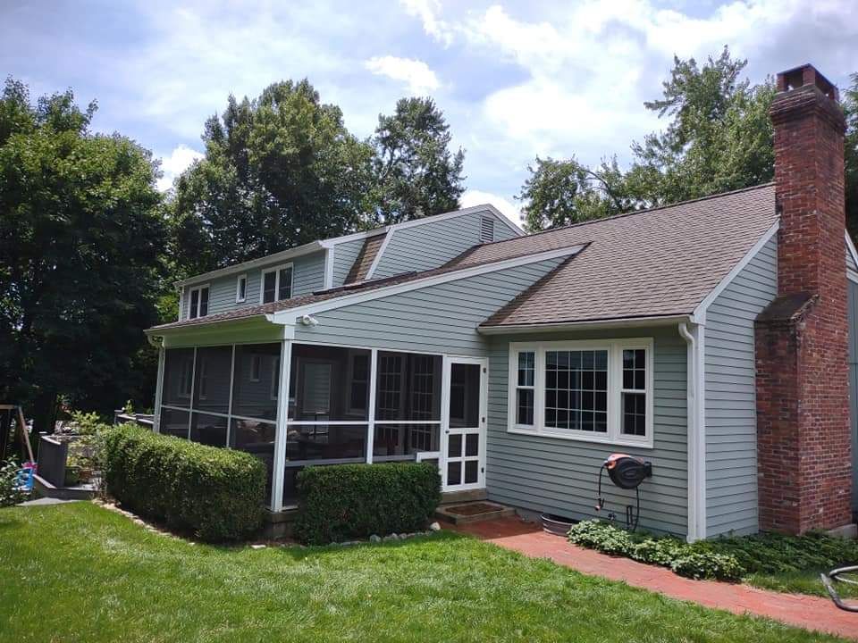 Green house with screened porch, gray siding, white trim, and a red brick chimney surrounded by trees.