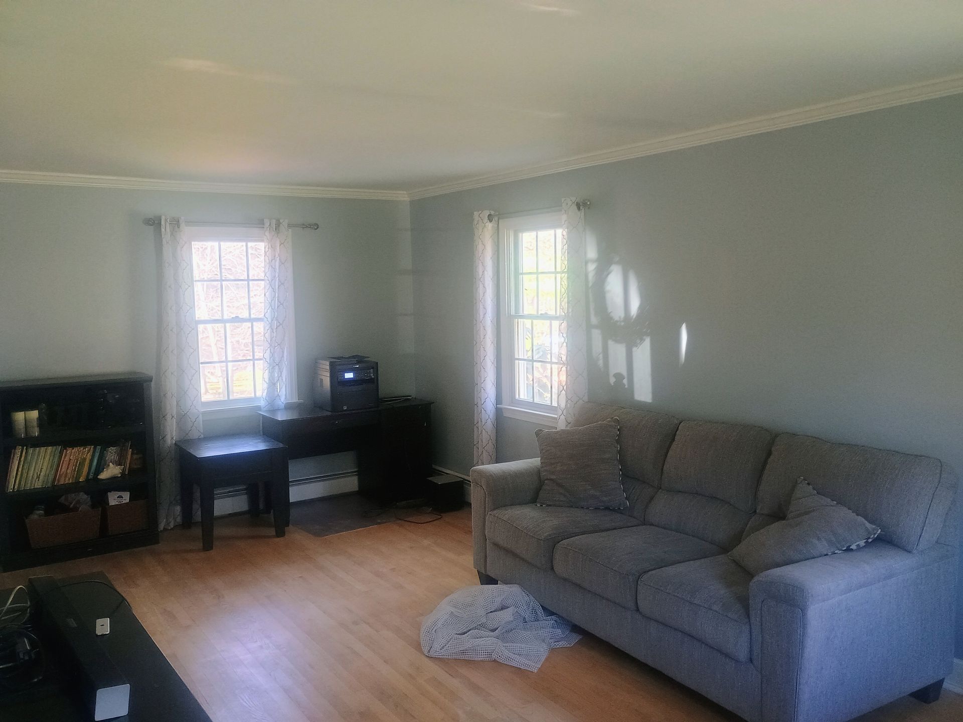 Bright living room with gray sofa, wood floor, two windows, and a small desk by the wall