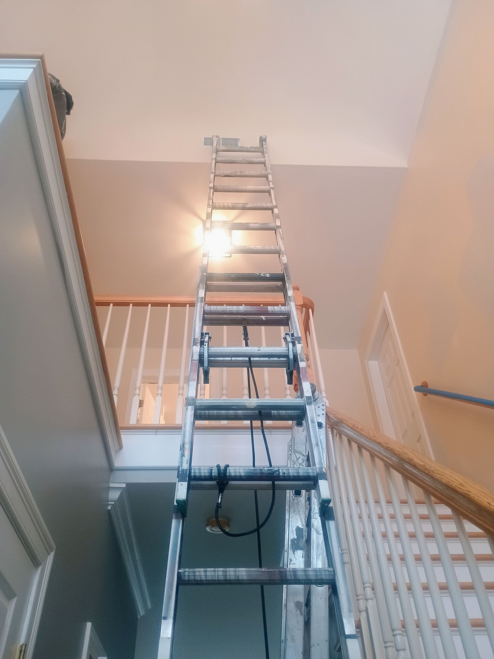 Extension ladder extended in a stairwell, reaching up toward the ceiling.