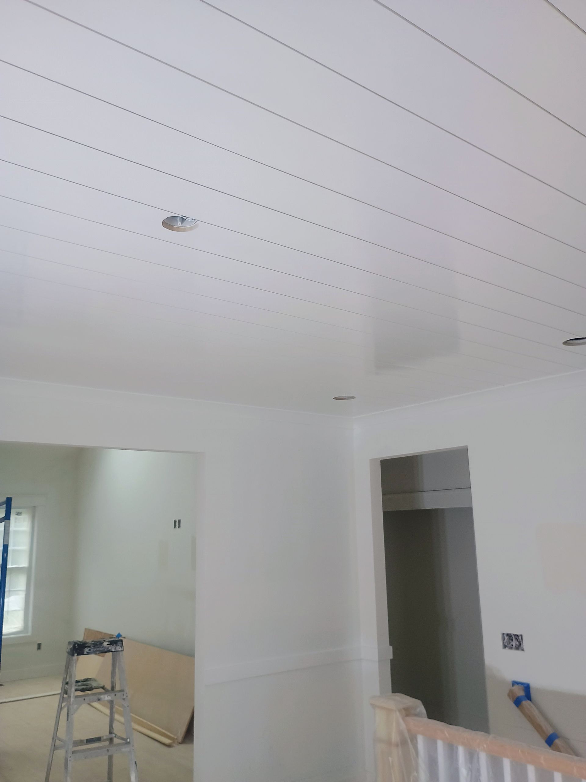 White room under construction with ladder, taped ceiling seams, and unfinished doorways