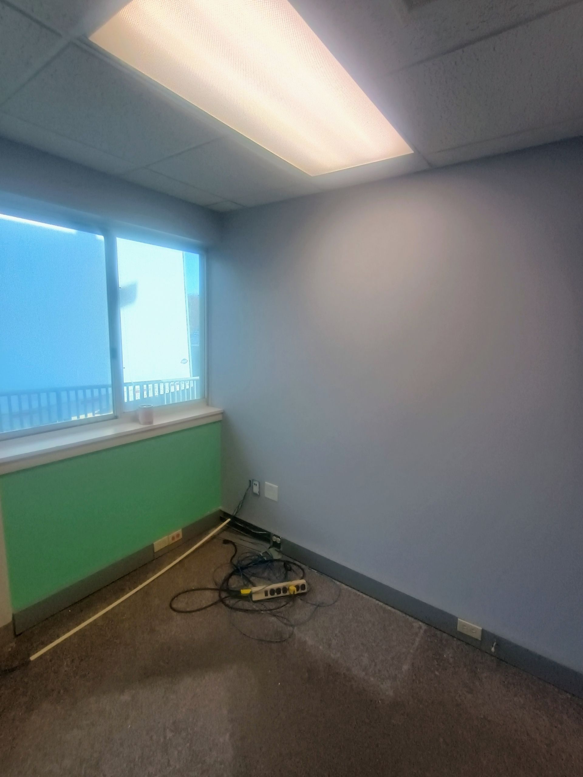 Empty office corner with a window, green radiator cover, and tools on the floor.