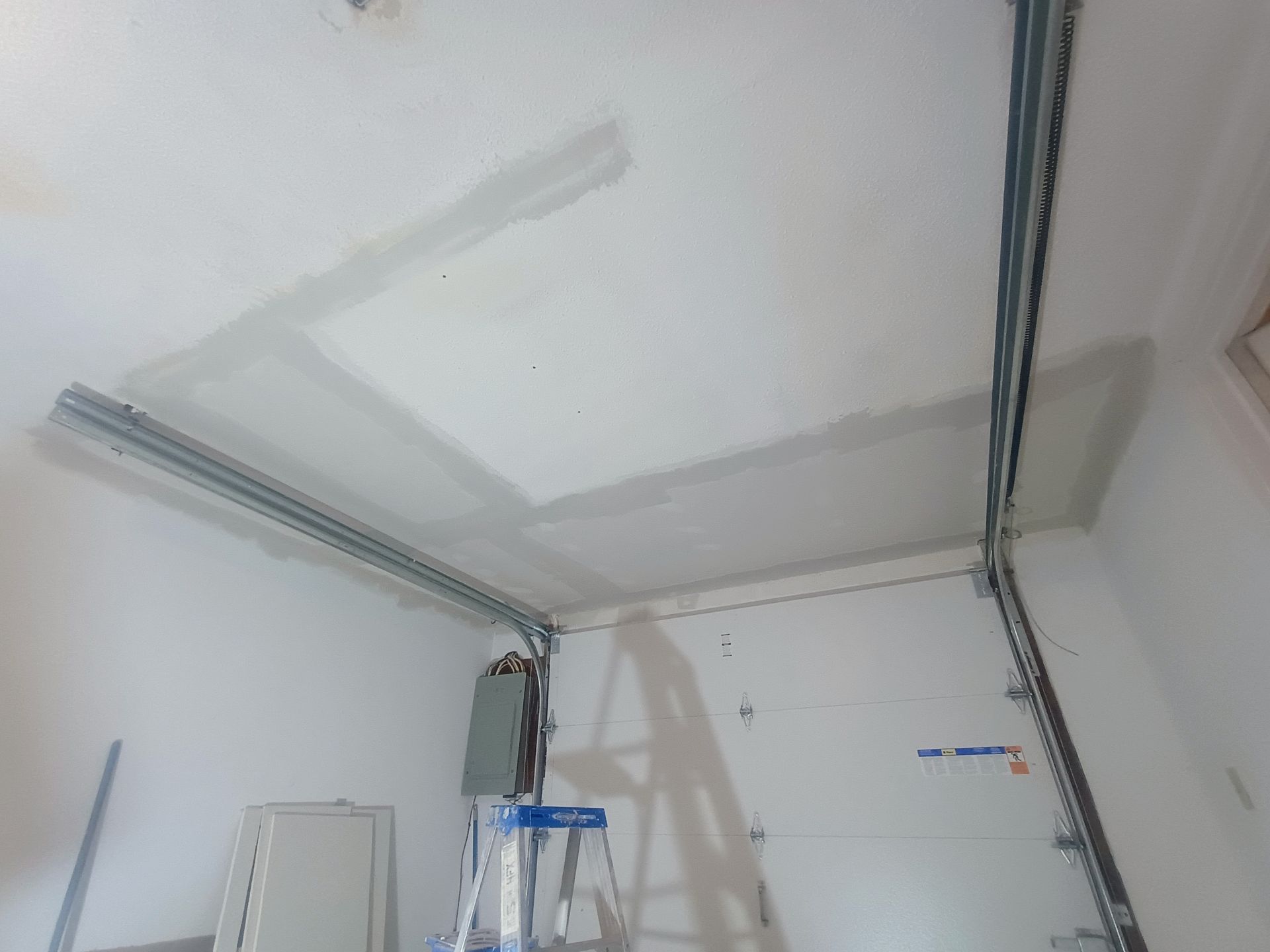Garage ceiling with metal tracks and a blue ladder in a white room