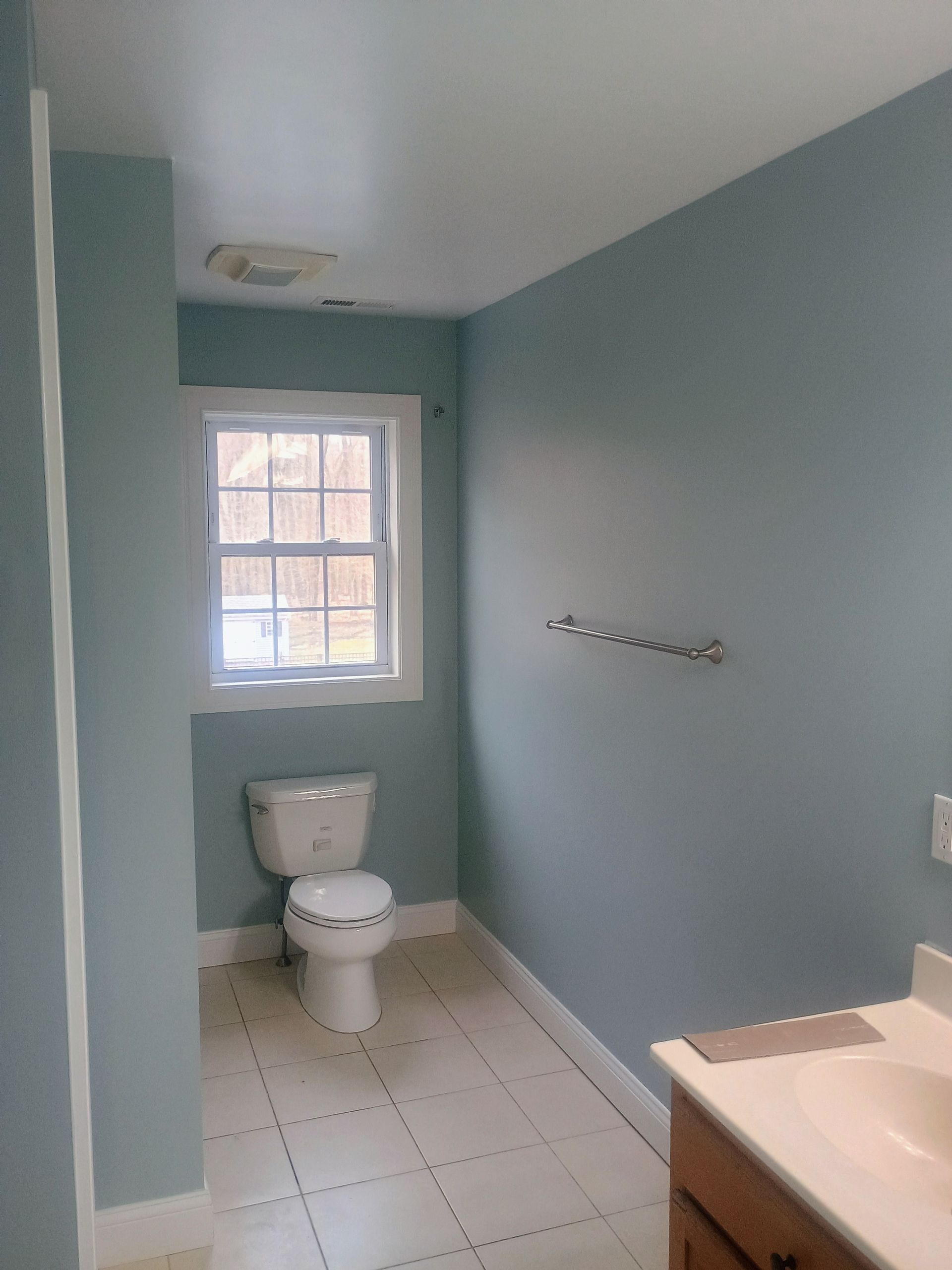 Small bathroom with toilet, window, light blue walls, and a sink counter on the right.