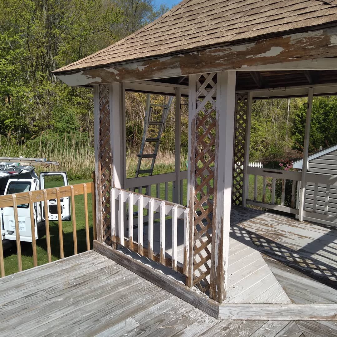 Wooden gazebo on a deck with white railings, overlooking a grassy yard and parked cars.