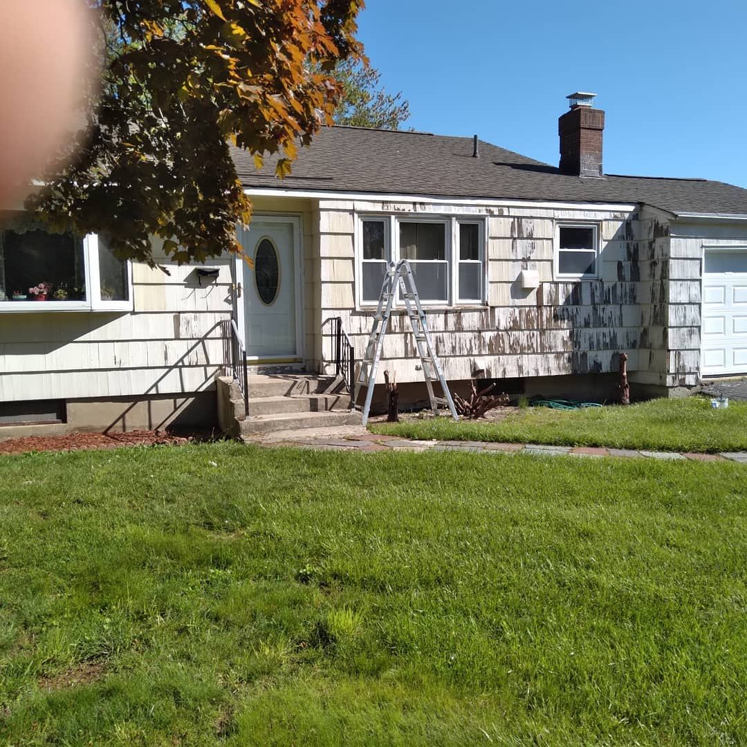 Single-story white house with front steps, lawn, and a ladder leaning against the porch in sunlight