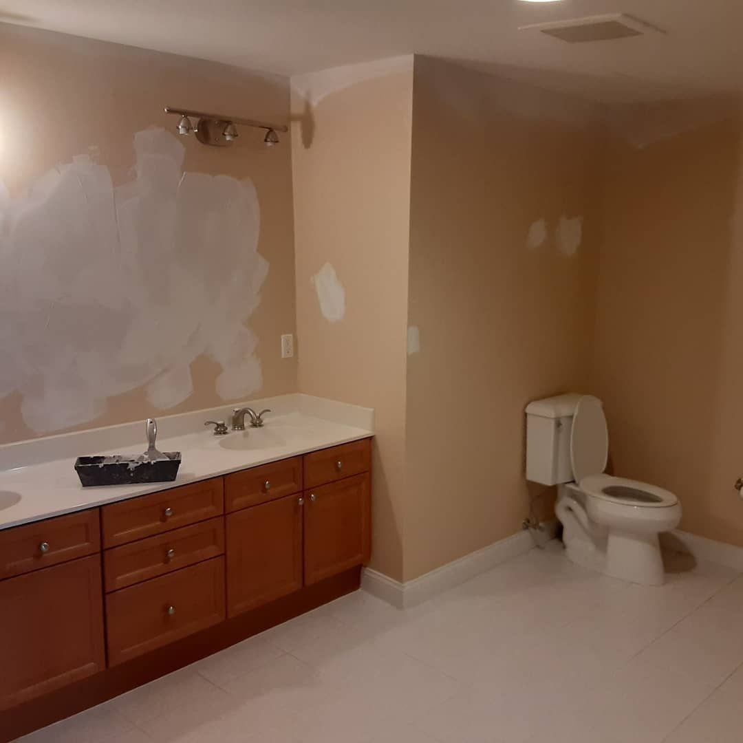 Bathroom with double vanity, toilet, and freshly patched beige walls under renovation