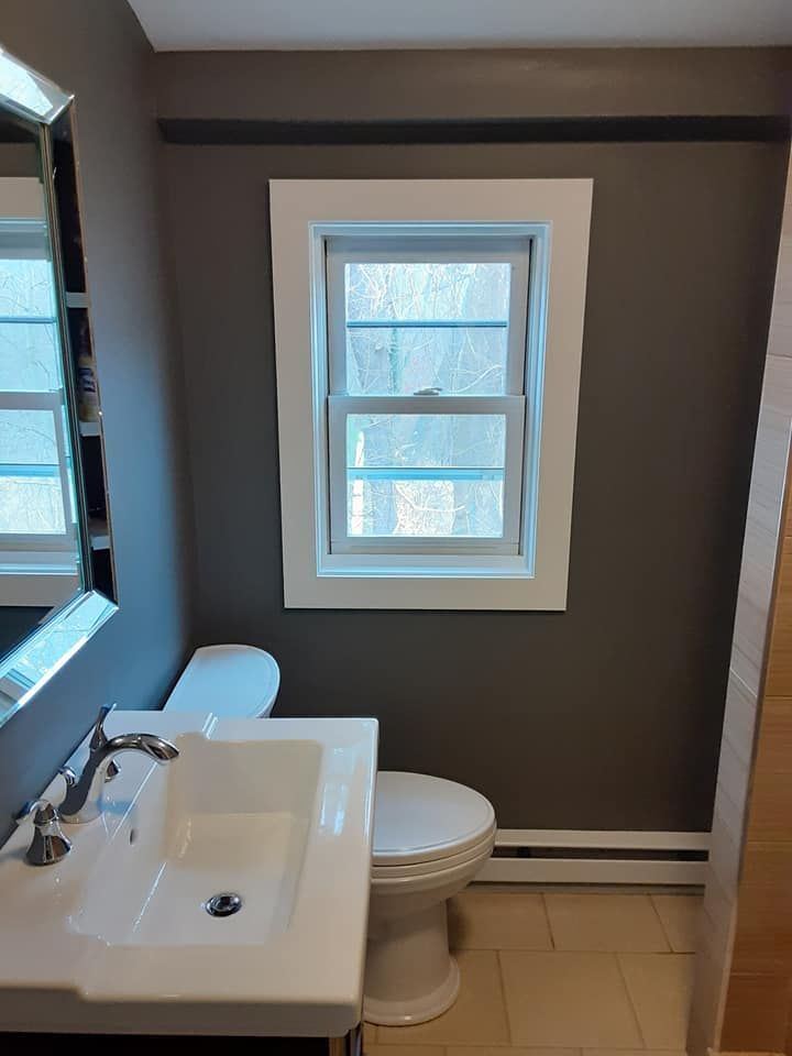 Small bathroom with sink, toilet, and window; gray walls, white trim, and beige tile floor.
