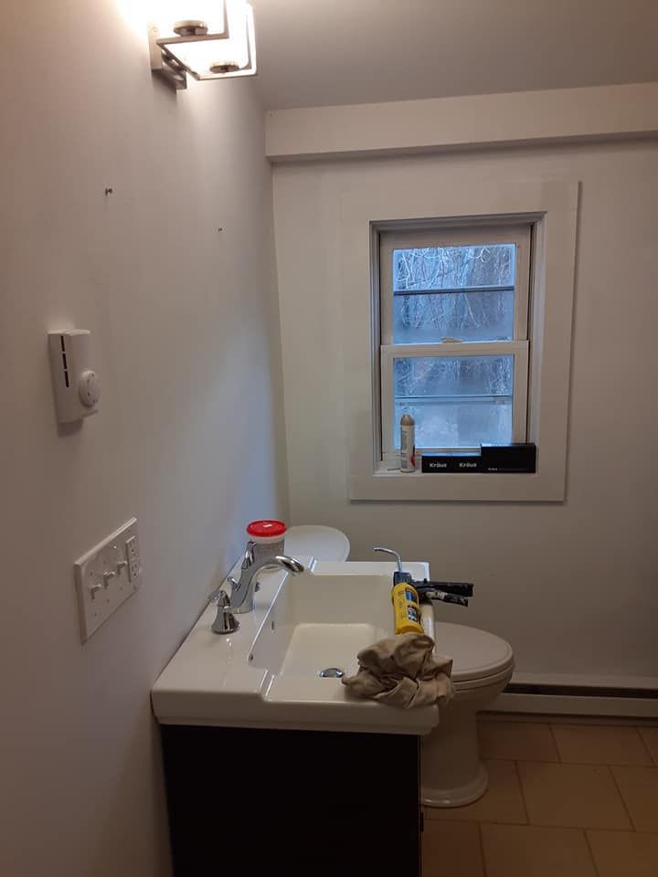 Small bathroom with a sink, toilet, wall light, and a window above the toilet.