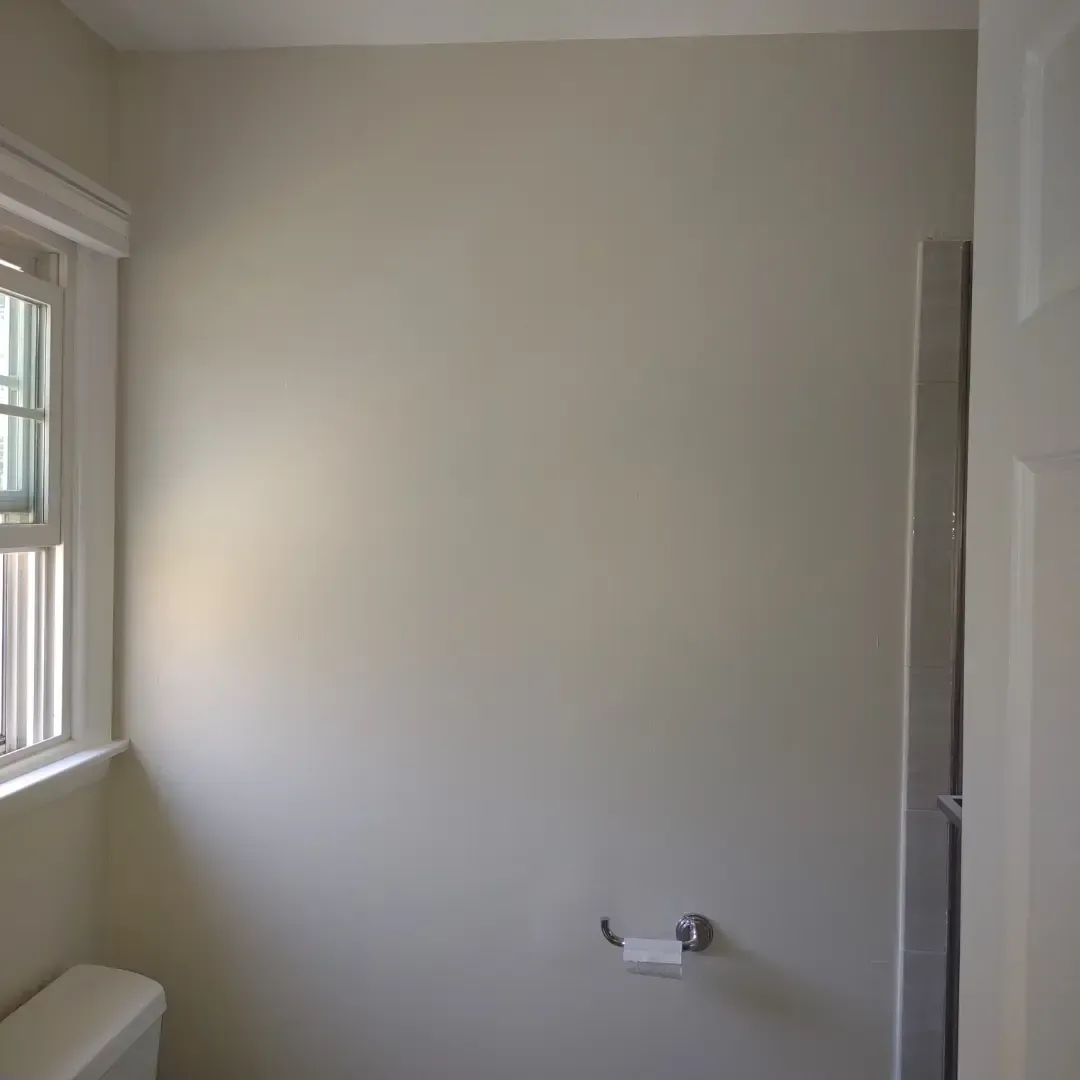 Small beige bathroom with a window, toilet paper holder, and shower stall doorway