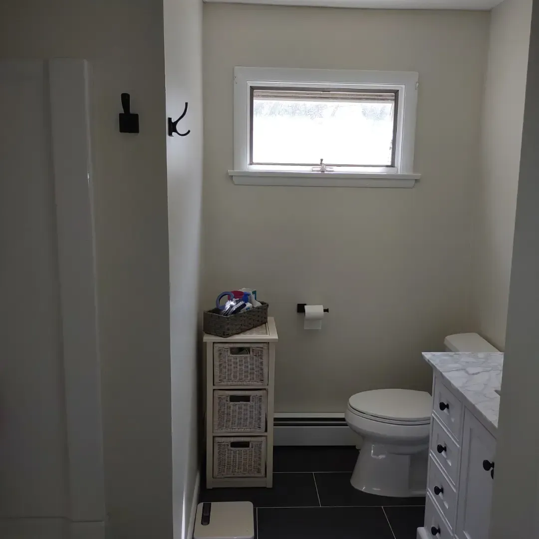 Small bathroom with toilet, window, wicker storage, and white vanity.