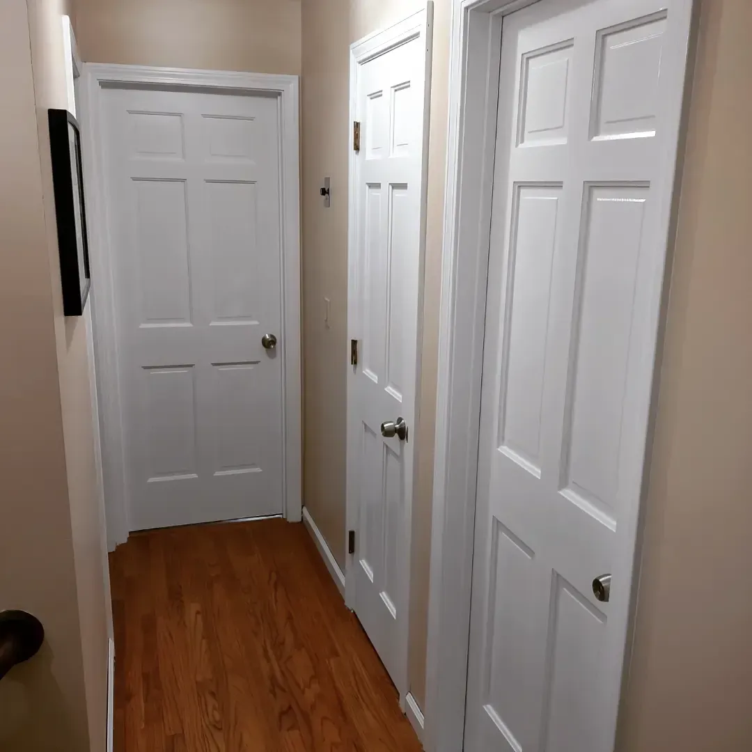 Narrow hallway with white doors, beige walls, and wood flooring