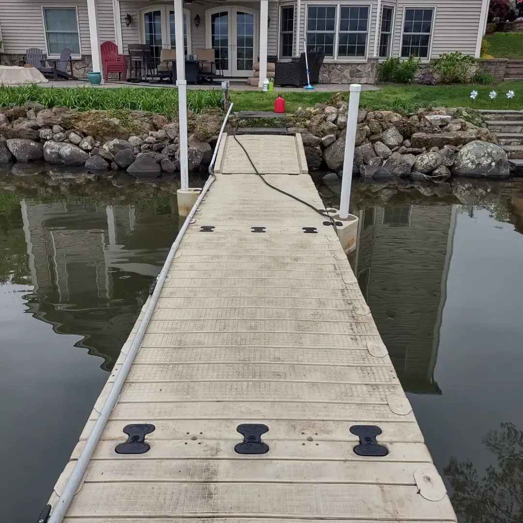 Wooden dock leading to a lakeside house, with rocky shoreline and calm water on both sides.