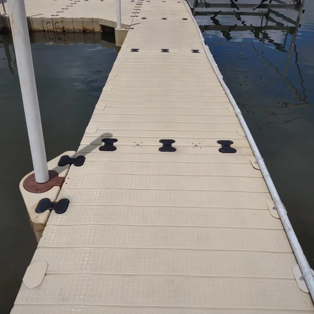Floating dock walkway with white planks and black mooring cleats over calm water.