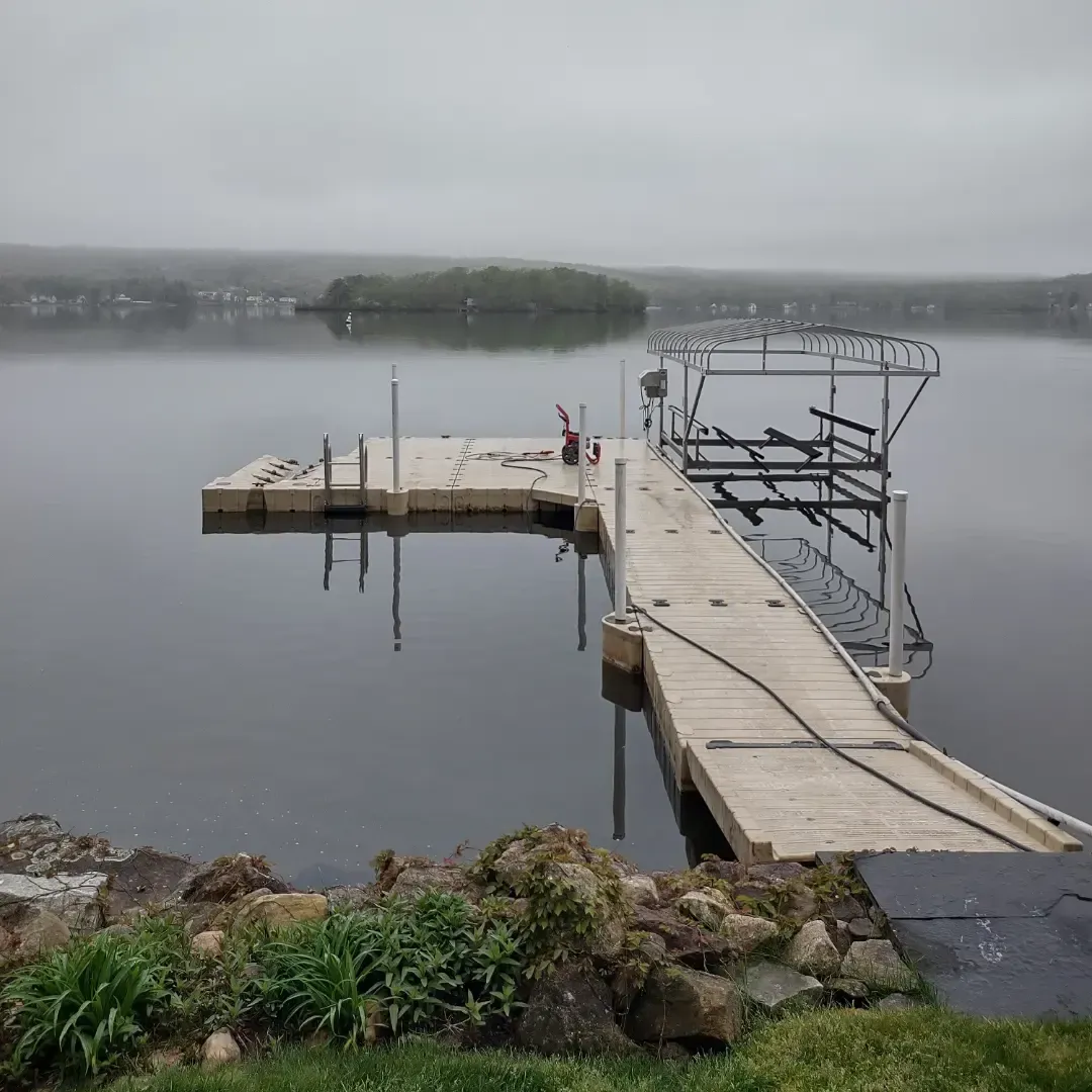 Foggy lakeside dock extending into calm water, with rocky shore and distant tree-covered island.