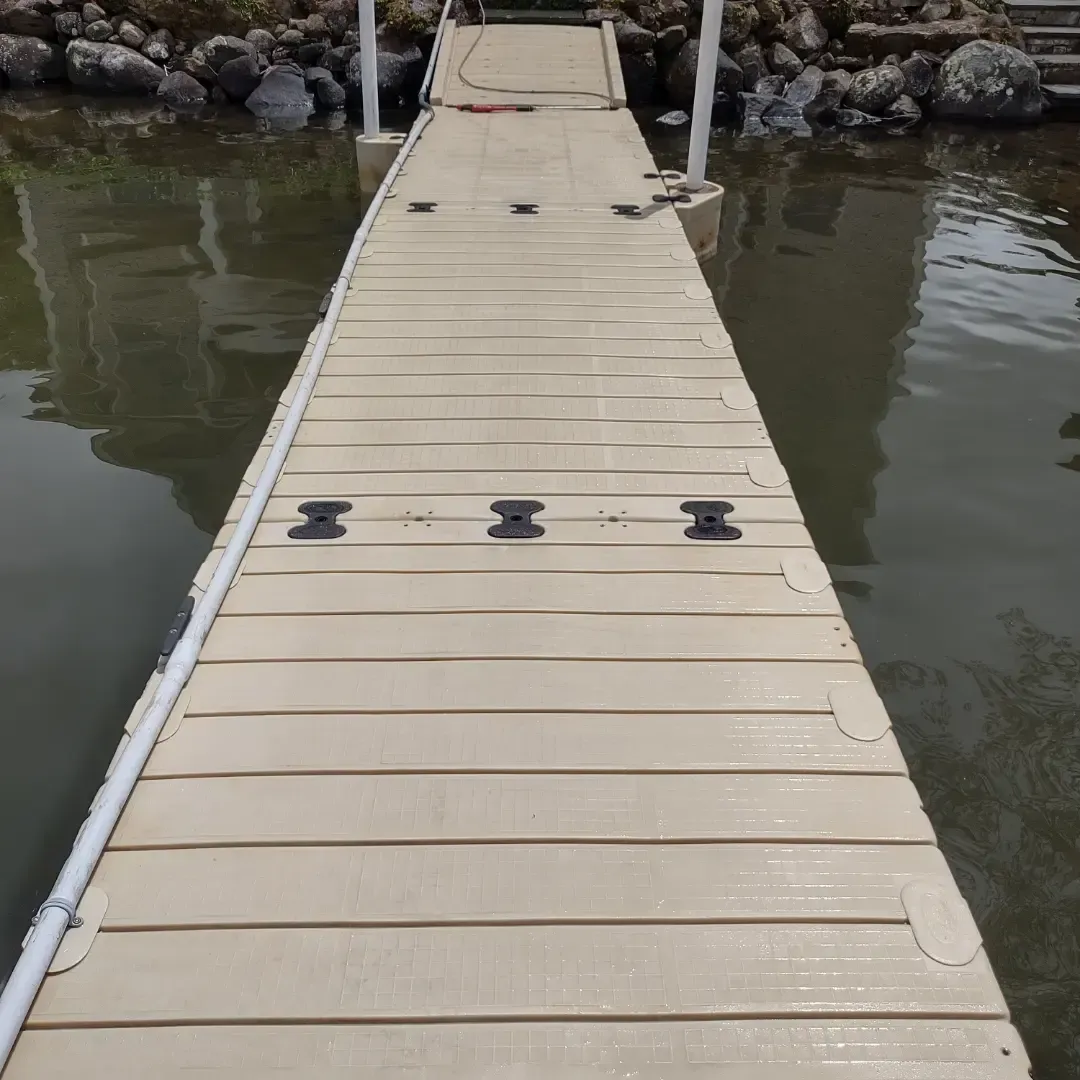 Beige dock walkway extending over calm water toward rocks and a shoreline
