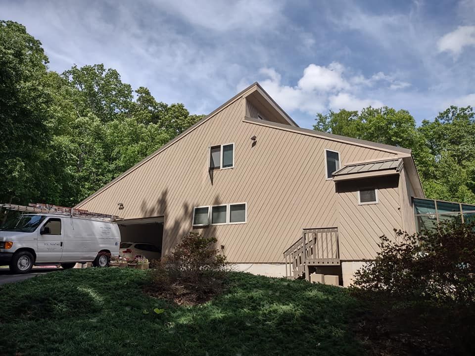 Beige house with a carport, white van, and trees under a partly cloudy sky