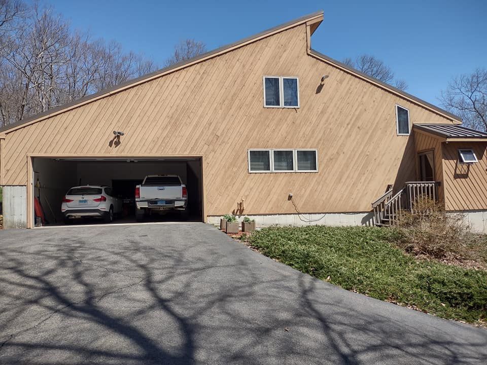 Wooden barn-style house with two cars in an open garage on a sunny day