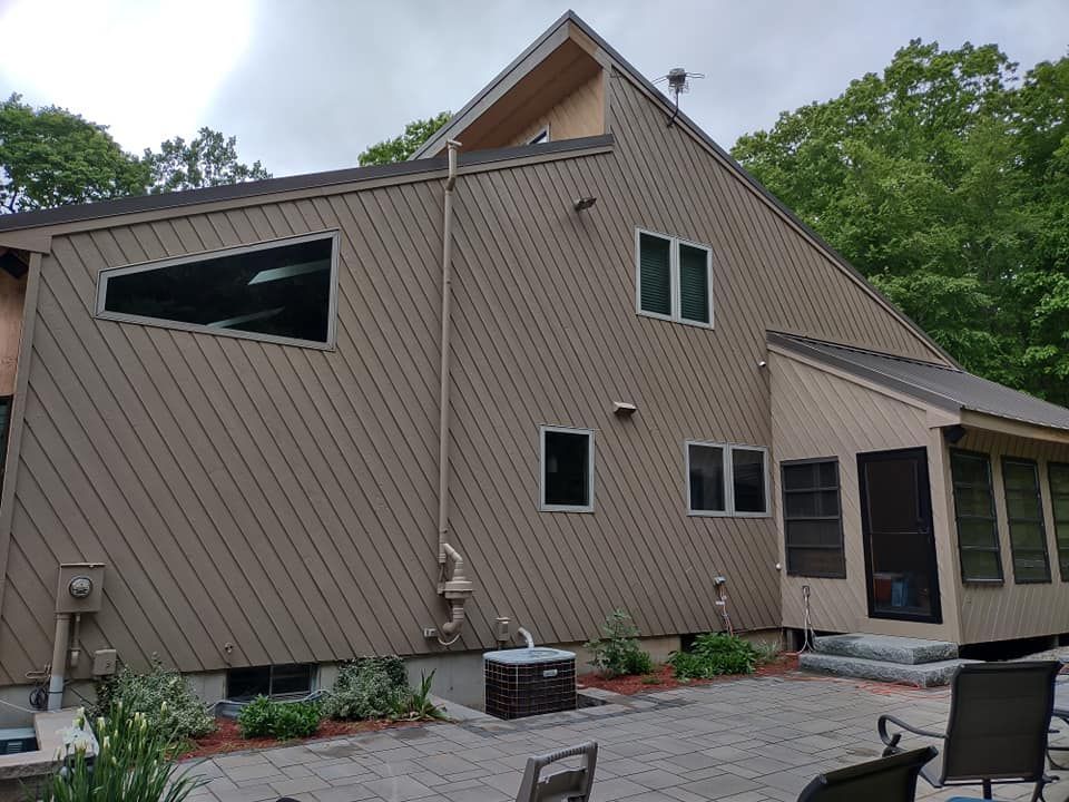 Modern house exterior with beige siding, slanted roof, small patio, and trees in the background