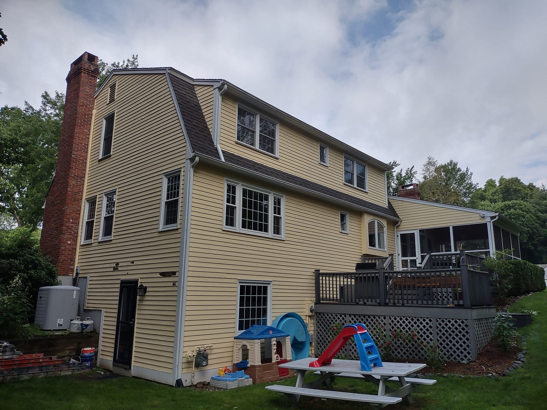 Three-story yellow house with brick chimney and children’s playset in a backyard.