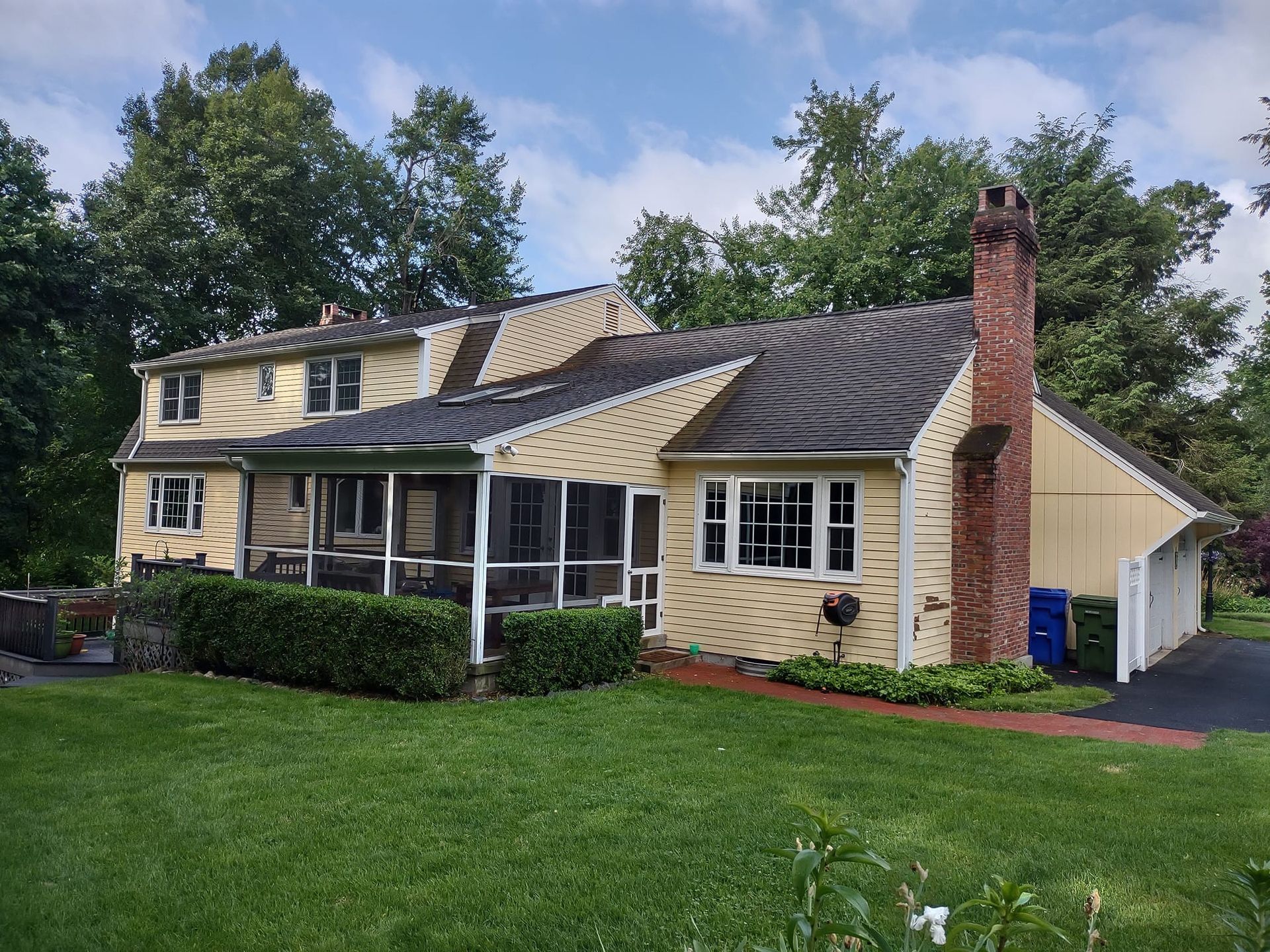 Person pressure-washing beige house siding beside a window