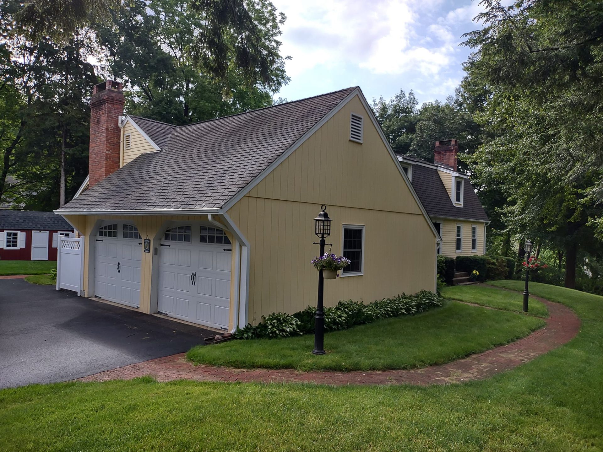 Yellow house with wavy roof, white garage doors, and a curved brick walkway amid green lawn and trees