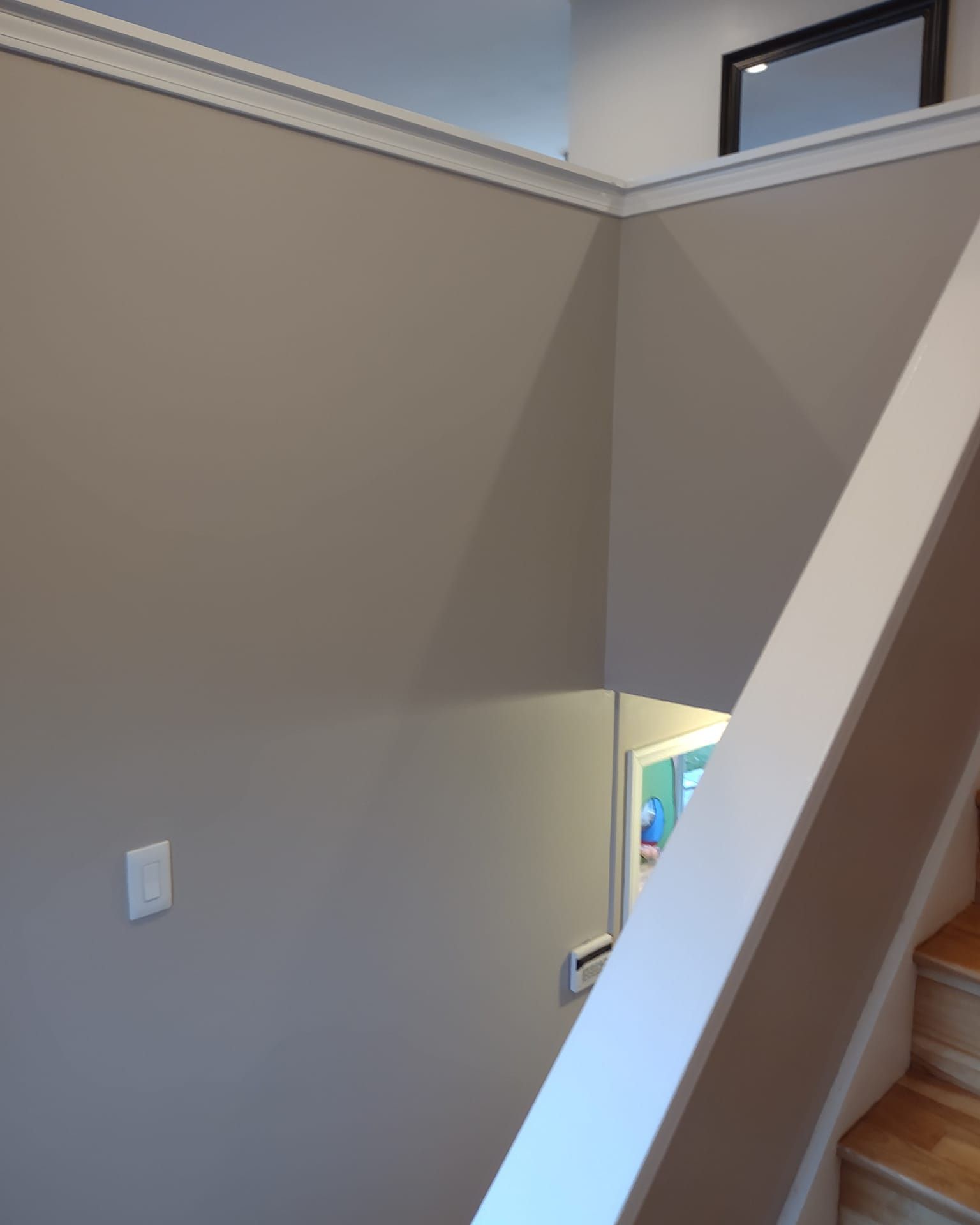 Interior stairwell with beige walls and a white railing beside wooden steps.